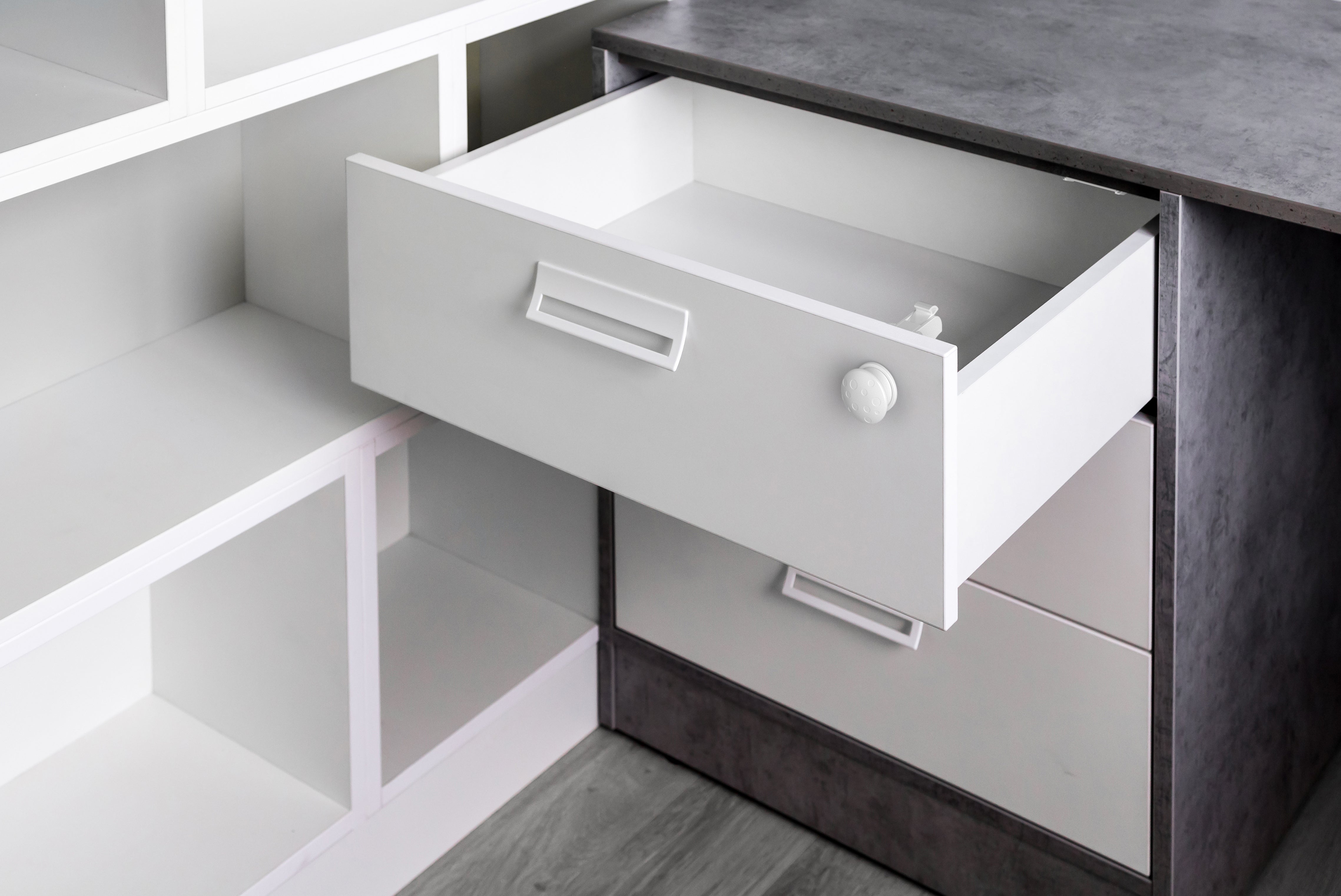 White drawer pulled open on dark grey kitchen cabinet unit with child safety lock on drawer front