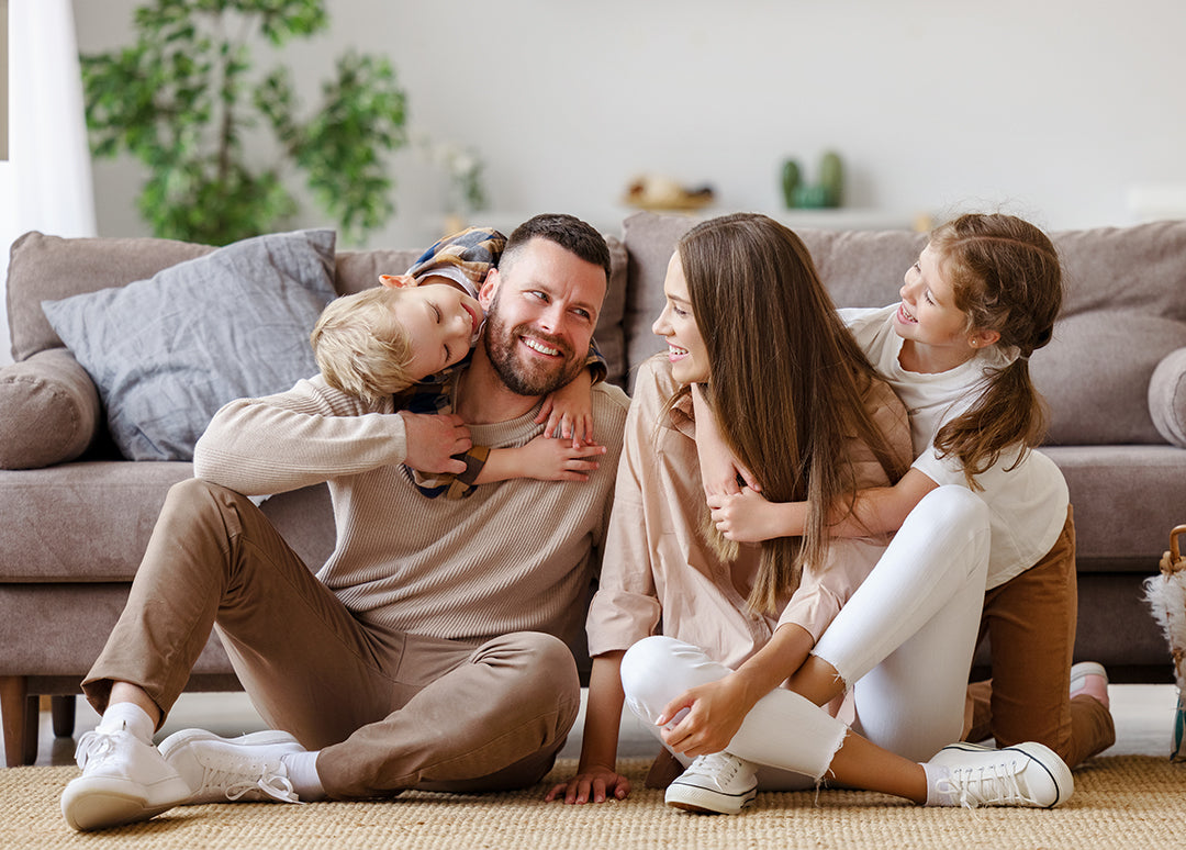 Two parents and two kids laughing together on living room floor, safe home ready for baby proofing bundles