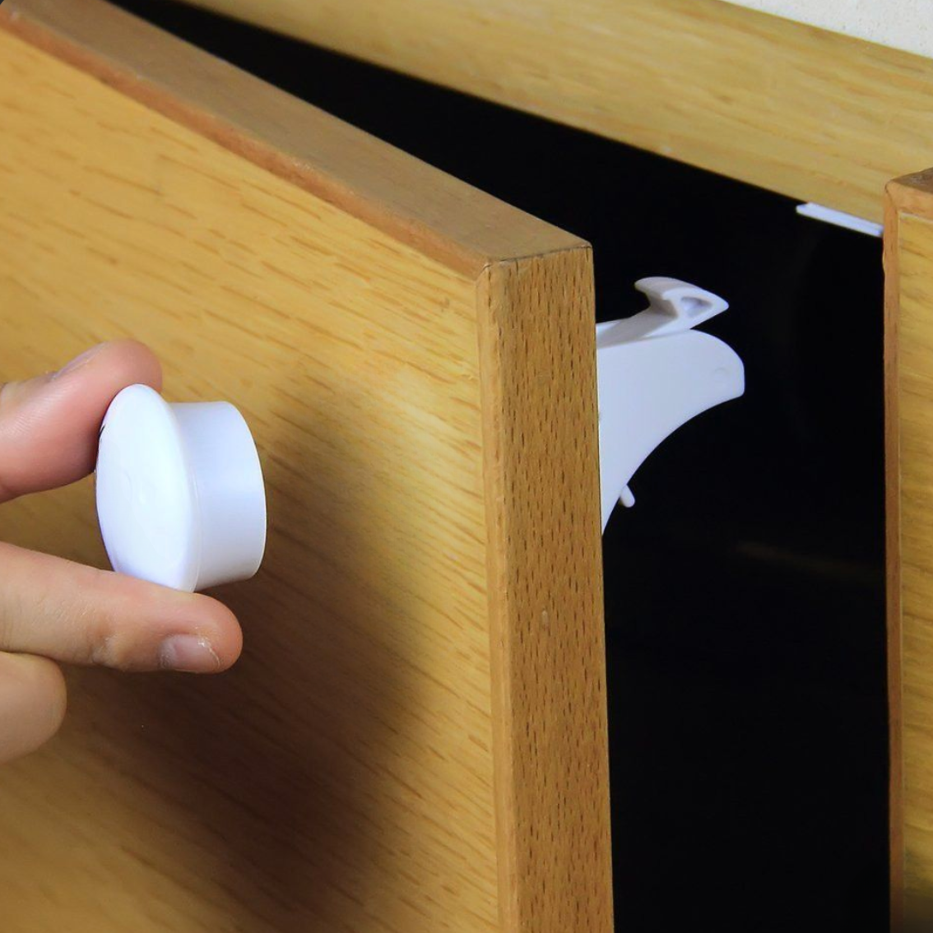 Parent holding magnetic key replacement against wood drawer front to disengage hidden cabinet lock inside