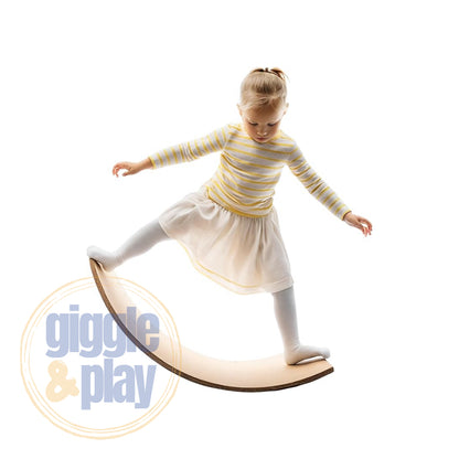Young girl balancing on one leg atop a curved wooden wobble board, arms out for balance